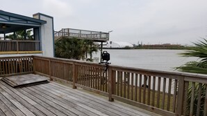 Une terrasse en bois offrant une vue sur une étendue d’eau calme, un espace abrité avec un toit bleu et un barbecue.
