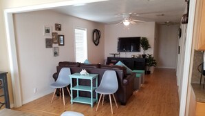 Un salon avec un canapé marron, deux fauteuils bleus, une petite table et un ventilateur de plafond.