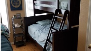 Une petite pièce comprenant un lit superposé, une petite étagère et une fenêtre avec des stores.
