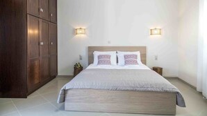 Un dormitorio con una cama grande, dos lámparas de pared, un armario de madera y una mesita de noche con una planta.