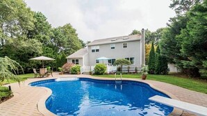 A swimming pool with a brick deck, surrounded by a grassy yard and trees. - Newly Renovated and Private Hamptons Home (Westhampton Beach)