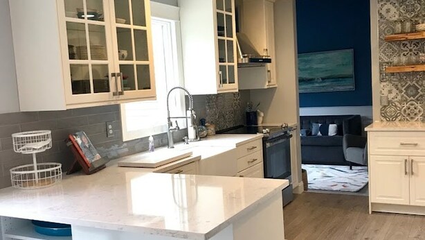 A modern kitchen with white cabinetry, a central island with bar stools, and a view into the living area. - Newly Renovated and Private Hamptons Home (Westhampton Beach)