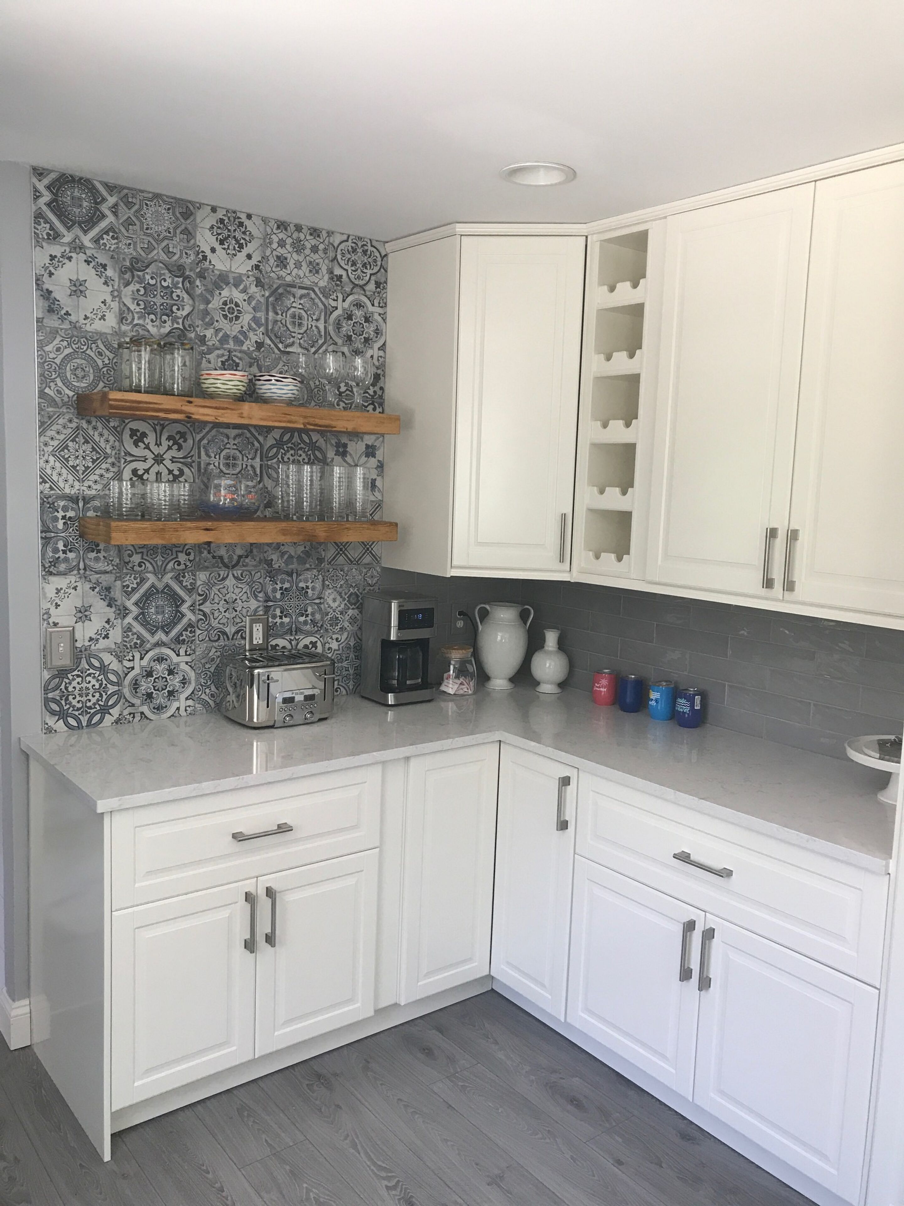 A kitchen with white cabinets, a patterned backsplash, and a wooden shelf with glassware.
