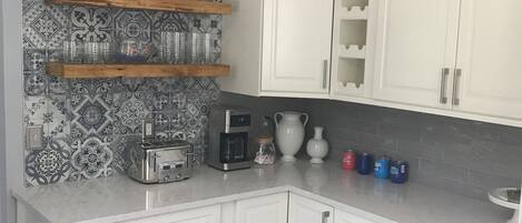 A kitchen with white cabinets, a patterned backsplash, and a wooden shelf with glassware.