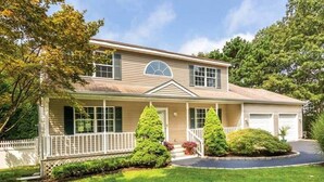 A two-story house with a front porch, a garage, and a well-maintained lawn. - Newly Renovated and Private Hamptons Home (Westhampton Beach)