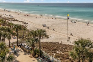 A beach with a flag, palm trees, and a patio area with outdoor seating.