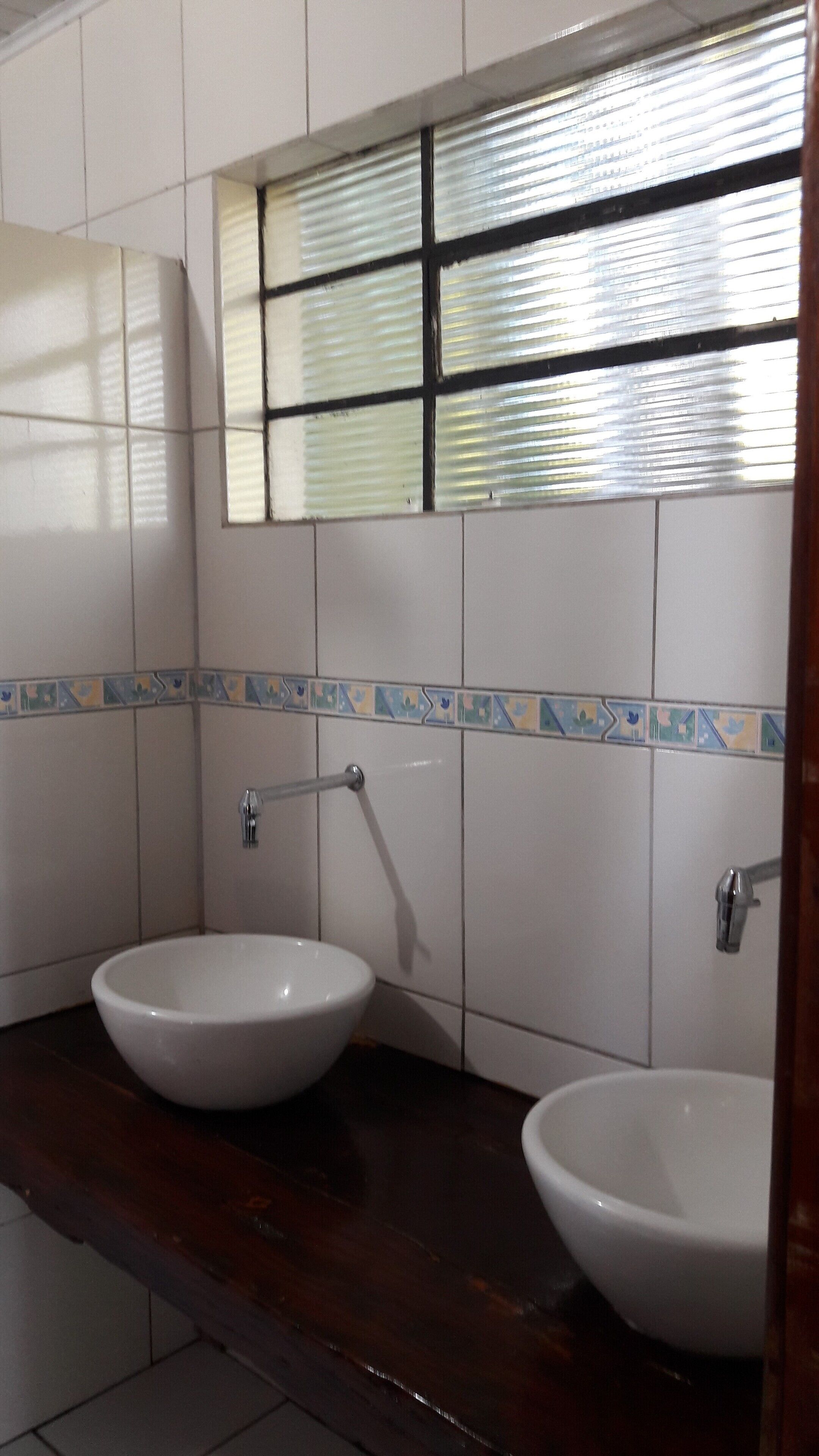 Une salle de bain avec deux lavabos blancs, un miroir et une fenêtre avec des stores.