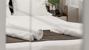 Uma cama bem arrumada com lençóis brancos, um travesseiro marrom escuro e um painel decorativo com padrão floral.