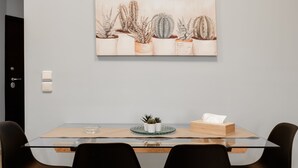 Uma sala de jantar com mesa de vidro, cadeiras pretas e um quadro decorado com tema de cactos na parede.