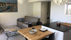 Un espacio habitable moderno con comedor, sofá, mesa de centro con revistas y un cuadro de un paisaje urbano.