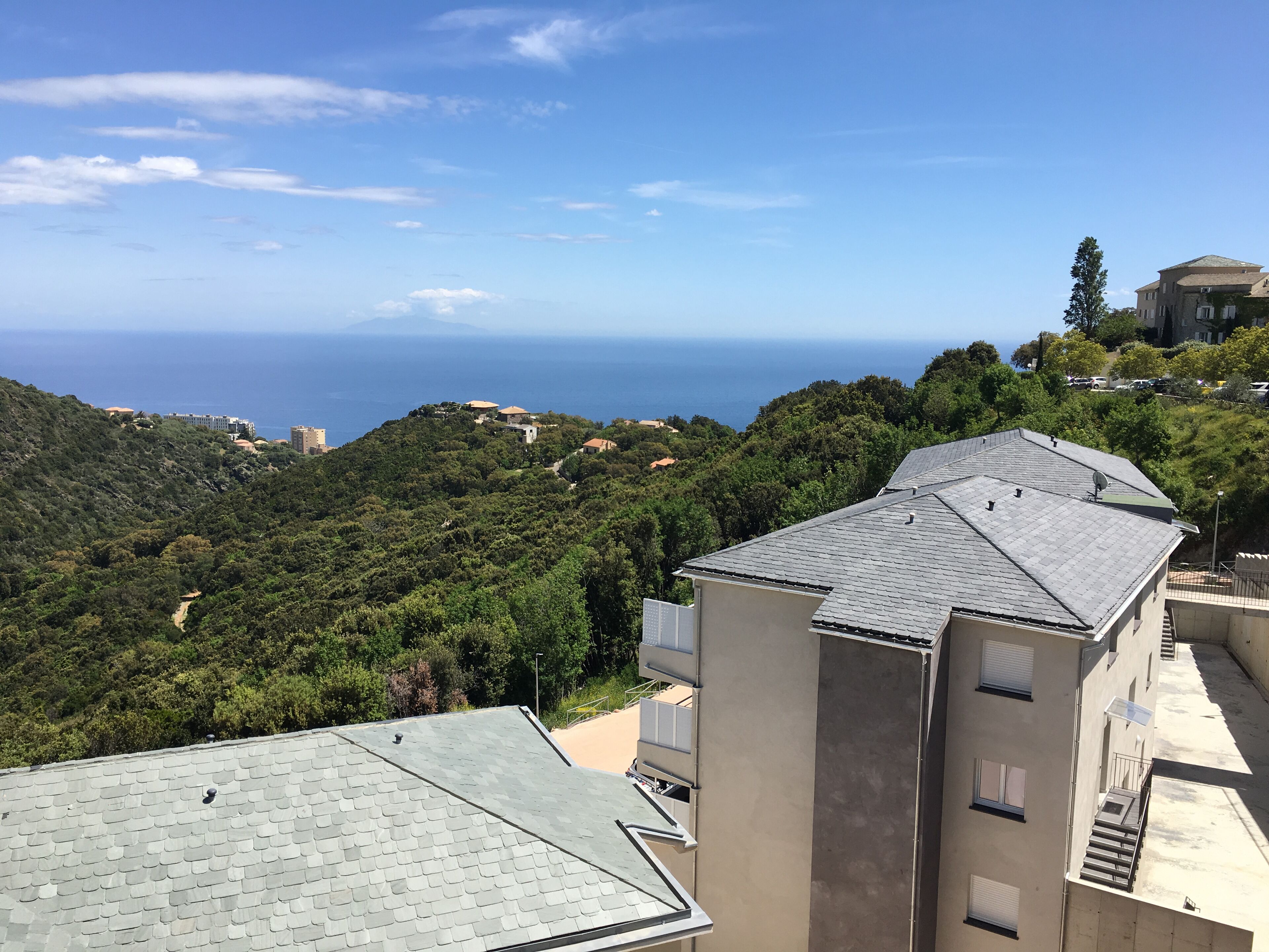 A building with a sloped roof, surrounded by lush greenery and a view of the sea.