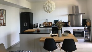 Una cocina moderna con una isla central, sillas negras, una lámpara colgante y electrodomésticos de acero inoxidable.