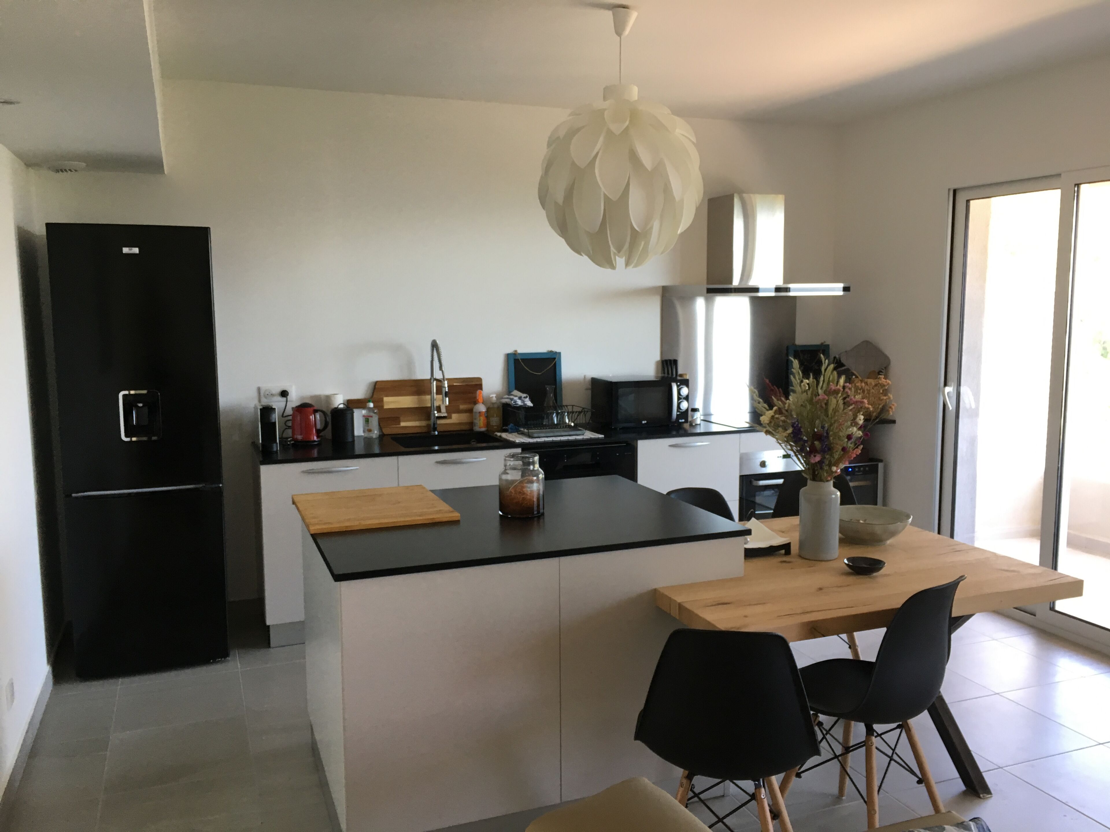 A modern kitchen with a central island, black appliances, and a wooden dining table with black chairs.