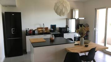 A modern kitchen with a central island, black appliances, and a wooden dining table with black chairs.