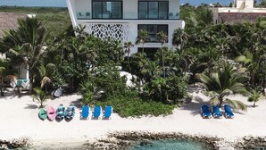 A modern beachfront property with a white building, clear blue waters, and several colorful lounge chairs. - Beachfront without seaweed, infinity pool, rooftop jacuzzi, Chef included. (TULUM)