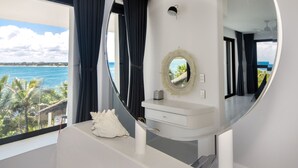 A modern bathroom with a large window, a round mirror, and a white vanity. - Beachfront without seaweed, infinity pool, rooftop jacuzzi, Chef included. (TULUM)