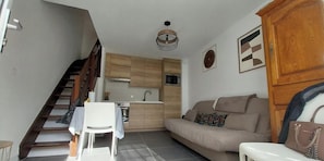 A compact living space with a kitchenette, a sofa, a dining table with chairs, and a staircase.