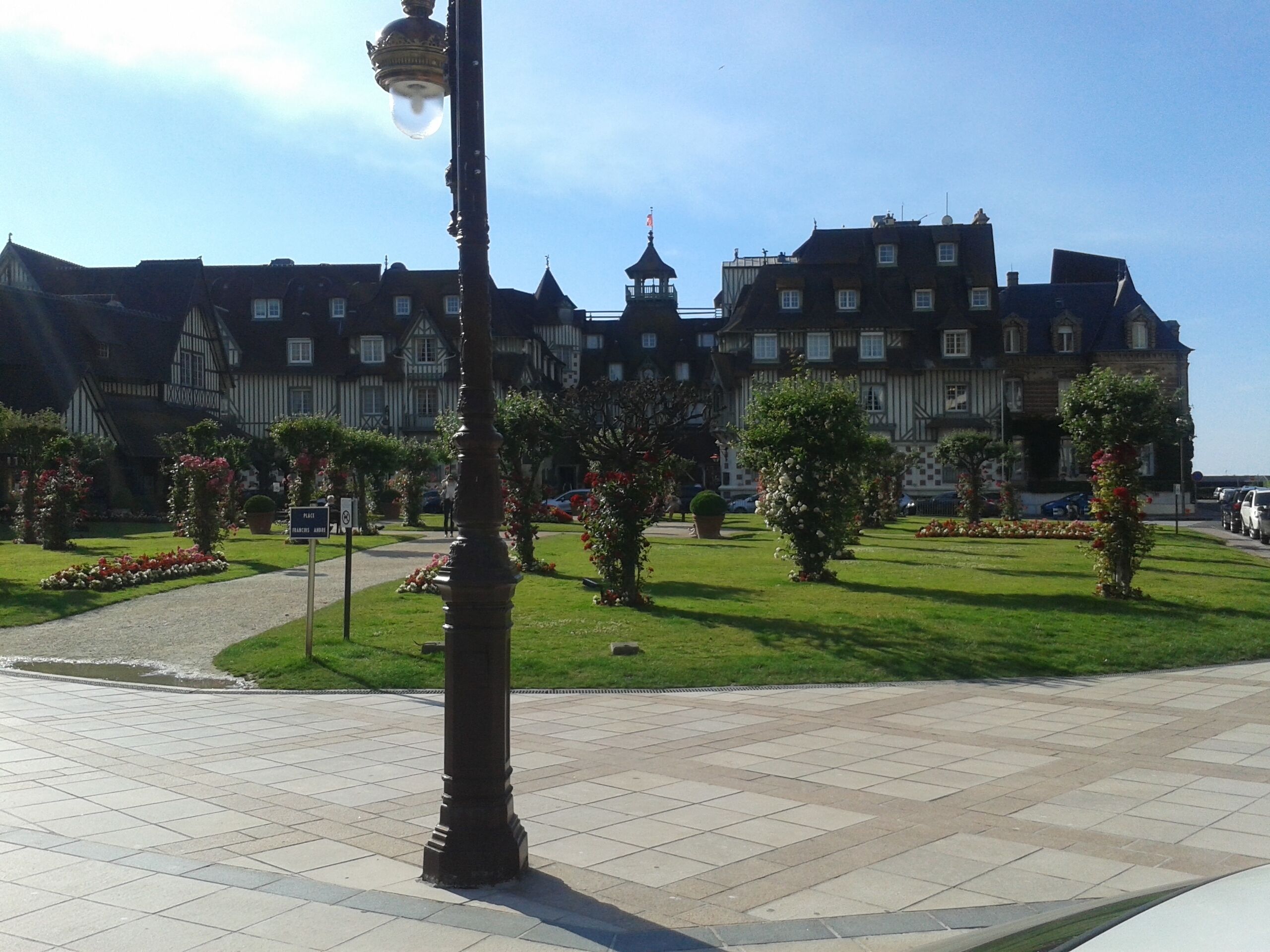 A large, historic building with a symmetrical facade, a central tower, and a well-maintained garden with pathways and flower beds.