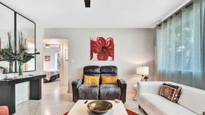A modern living room with a black leather sofa, a white couch, a coffee table, and a red flower painting on the wall. - Heated pool, parking, 5 min walk to food and fun! (Wilton Manors)