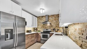 A modern kitchen with stainless steel appliances, a stone backsplash, and a white countertop. - Heated pool, parking, 5 min walk to food and fun! (Wilton Manors)