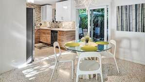 A modern kitchen with white cabinets, a stainless steel refrigerator, and a dining area with a glass table and white chairs. - Heated pool, parking, 5 min walk to food and fun! (Wilton Manors)