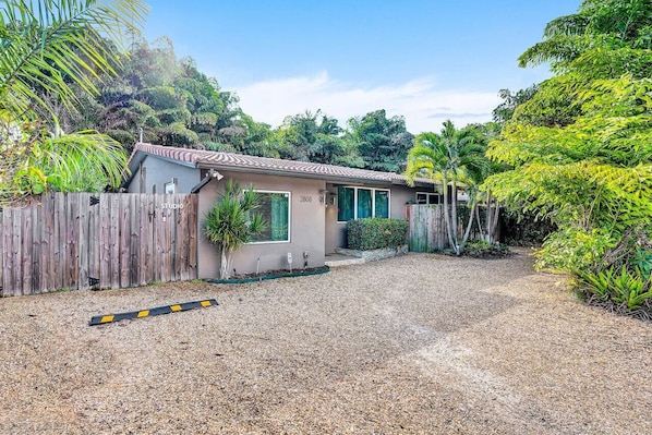 Une maison de plain-pied avec un toit en tuiles, une clôture en bois et une allée gravillonnée.