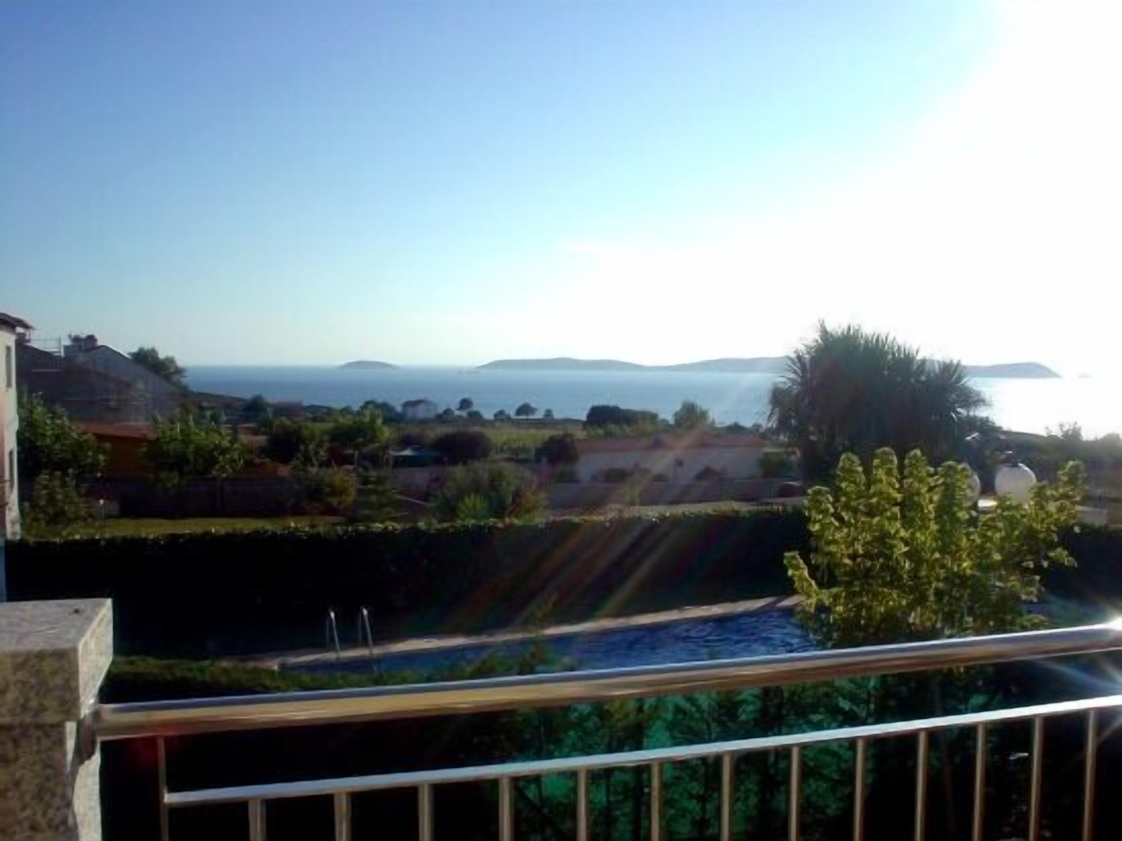 A coastal view from a balcony with a railing, overlooking a body of water and distant landforms.