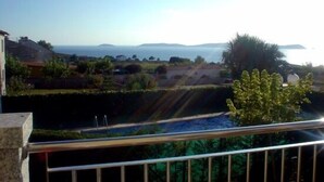 Vista costera desde un balcón con barandilla, sobre un cuerpo de agua y formaciones terrestres a lo lejos.