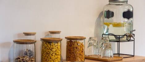 Un comptoir de cuisine sur lequel se trouvent divers bocaux en verre contenant différents aliments, un grand bocal en verre avec un couvercle en métal, et un présentoir en métal avec plusieurs verres.