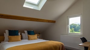 Une chambre avec un puits de lumière, un grand lit avec de nombreux oreillers, une tête de lit en bois, une fenêtre avec vue et une petite table.