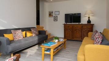 Ein Wohnzimmer mit grauem Sofa, gelbem Sofa, Couchtisch aus Holz und einem Fernseher auf einer Holzkommode.
