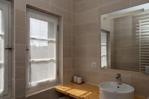 A bathroom with beige tiles, a wooden vanity, a white sink, and a window with blinds.