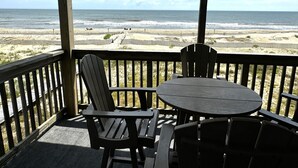 A wooden deck with a table and chairs overlooking a beach with a wooden fence. - Oceanfront 2BR/2 Bath Second Floor Condo with Pool and Oceanfront Deck (Rodanthe)