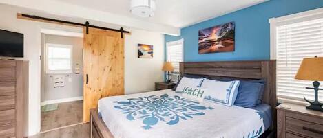 Un dormitorio con cama, cabecera de madera, mesitas de noche y televisor.