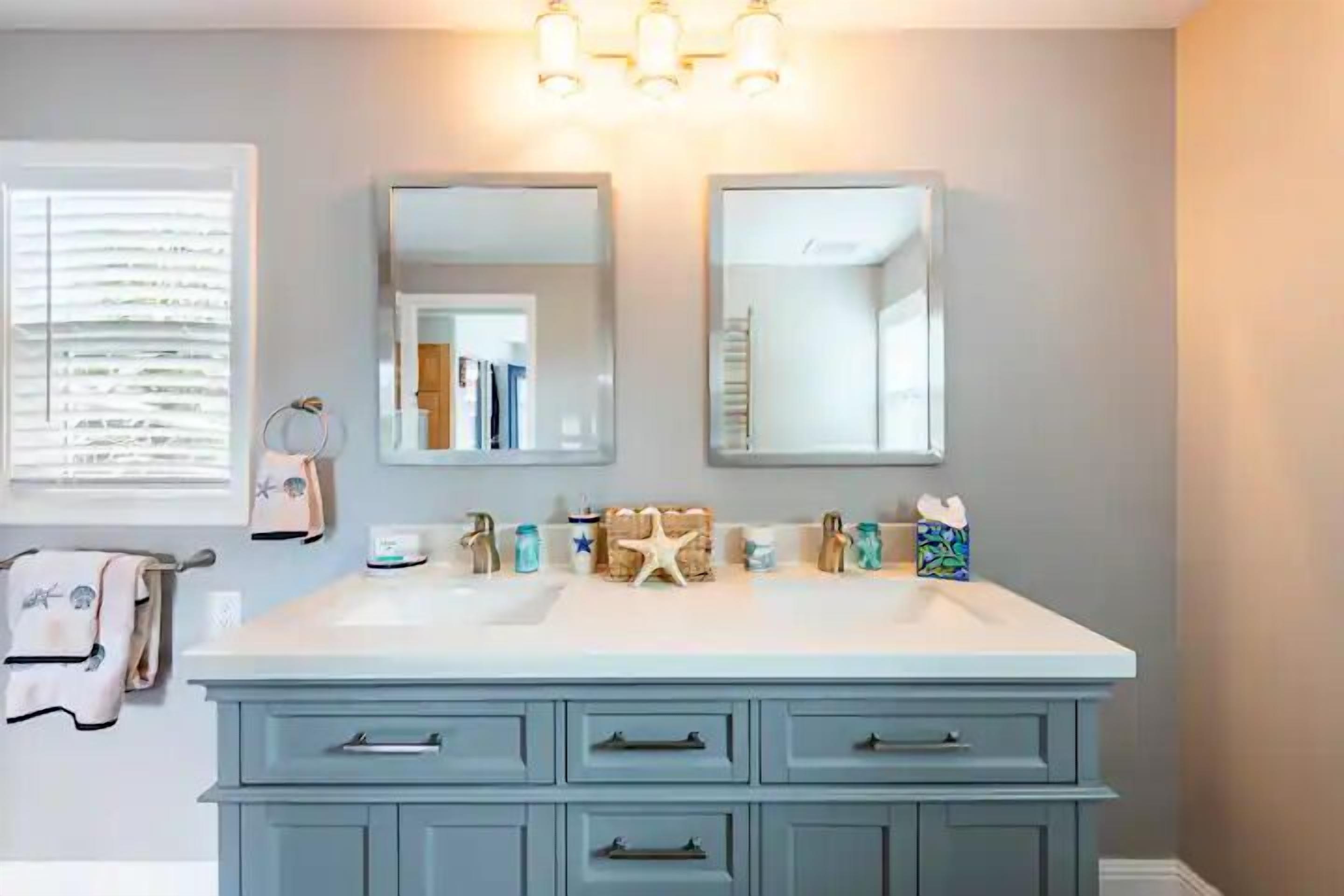 Un bagno con un mobile lavabo doppio, due specchi e un lampadario sopra il lavabo.