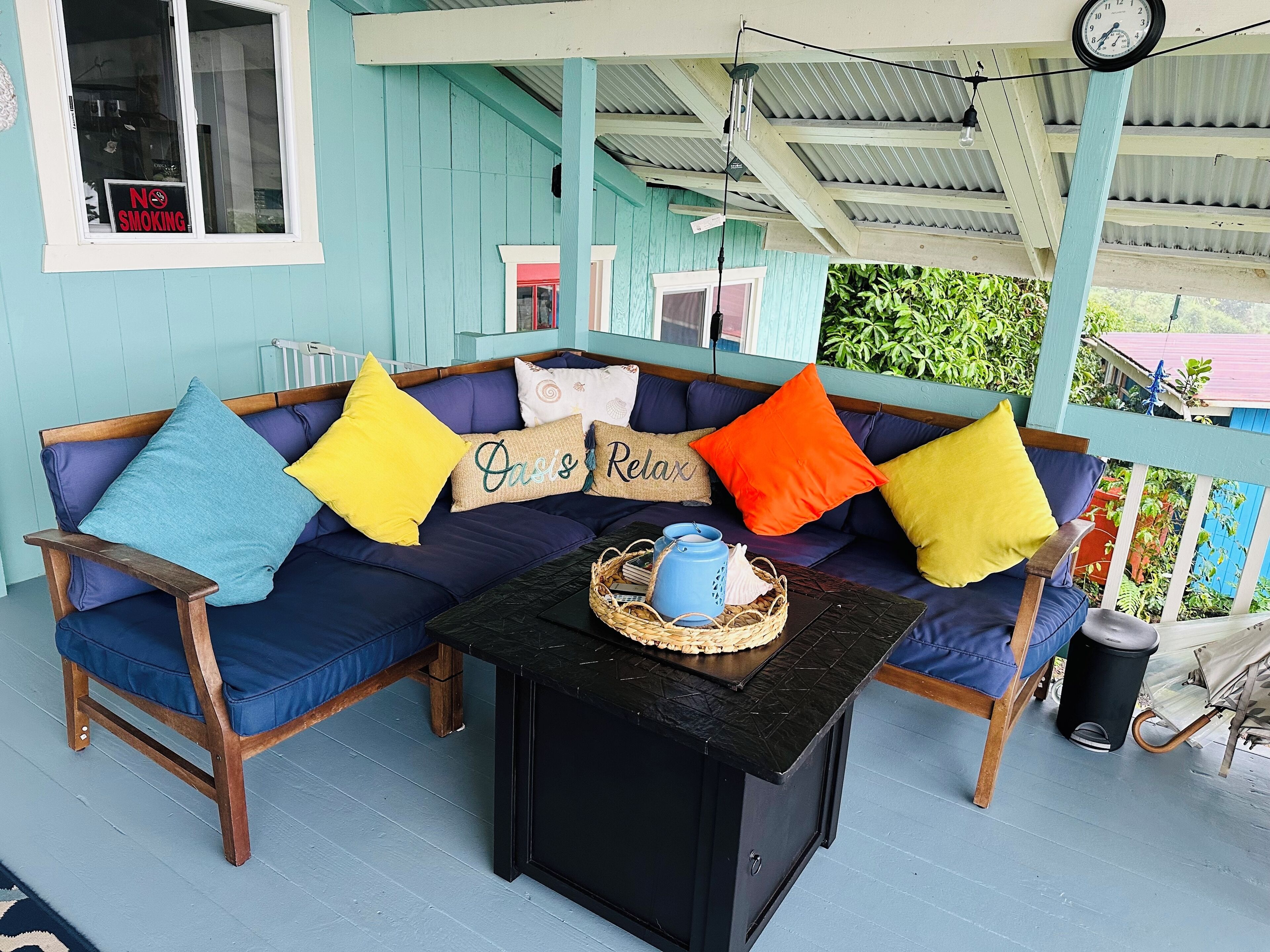 A cozy outdoor seating area with a blue sofa, a small table, and a clock on the wall.