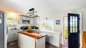 Een moderne keuken met witte kasten, een houten eiland, een zwart omrande magnetron en een zwarte deur.