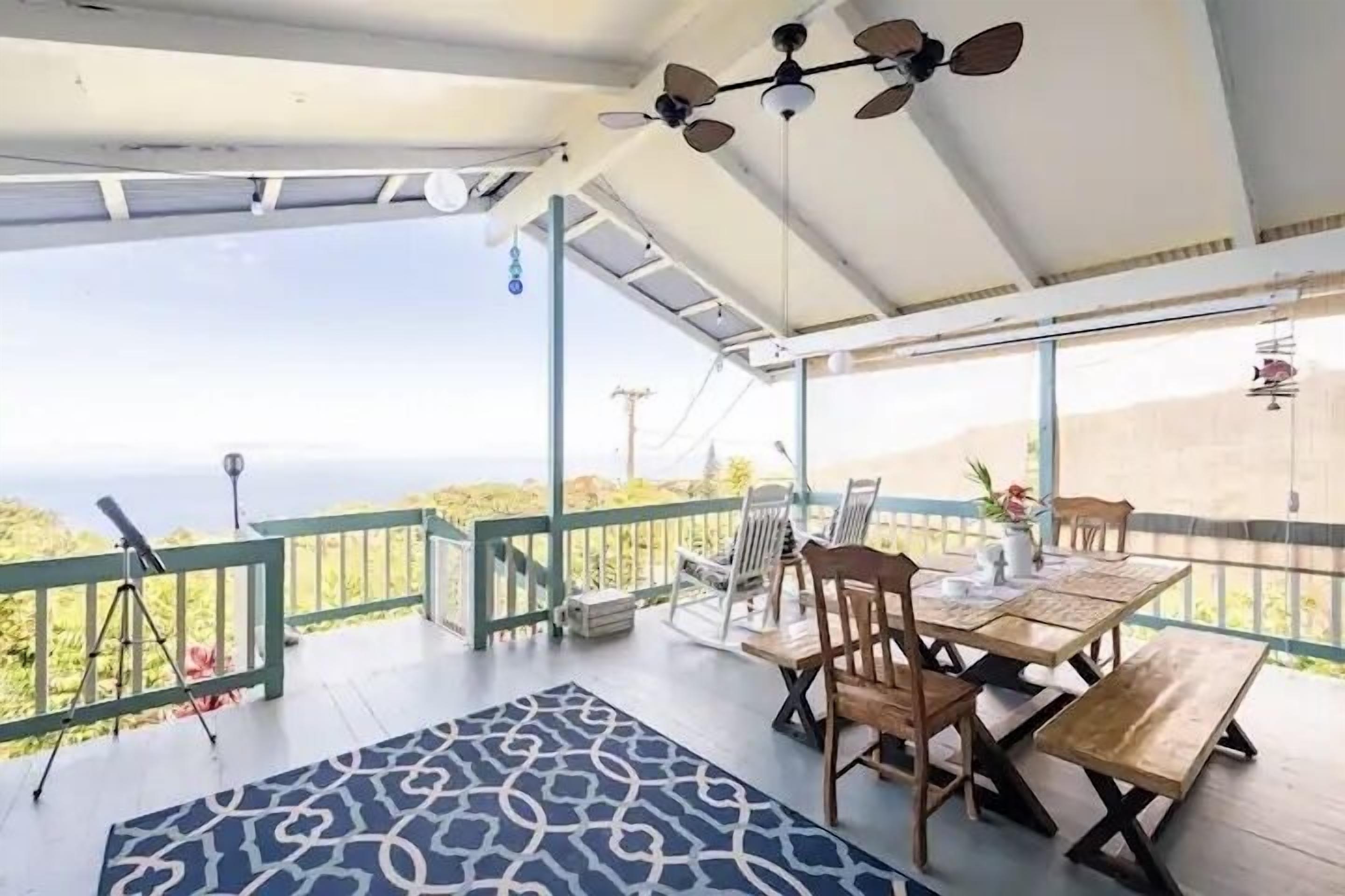 A covered outdoor area with a table and chairs, a telescope, and a view of the landscape.