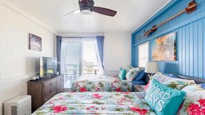 Een slaapkamer met een bed, een plafondventilator, een dressoir, een televisie en een raam met gordijnen.