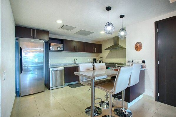 A modern kitchen with stainless steel appliances, a dining area with a table and chairs, and pendant lighting.