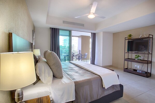 A hotel room with a bed, a desk, a chair, a TV, and a balcony with outdoor seating.