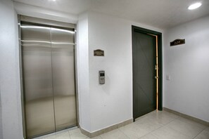 A hallway with two elevator doors, one metallic and one dark, and a wall-mounted emergency phone.