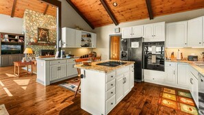 A spacious kitchen with white cabinets, a stone fireplace, and a large island with a built-in stove. - Discover Bear Trail in Boone, NC—a cozy 4-bedroom chalet perfect for 8 guests. (Boone)