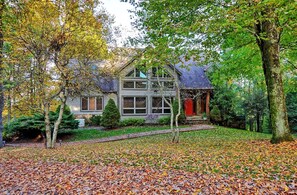 A two-story house with a red door, surrounded by trees and a leaf-covered lawn.