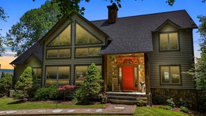 A two-story house with a stone facade, large windows, and a red door. - Discover Bear Trail in Boone, NC—a cozy 4-bedroom chalet perfect for 8 guests. (Boone)