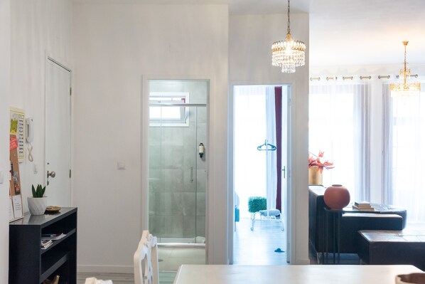 Una habitación de hotel moderna con puerta de ducha de vidrio, un área de comedor con mesa y sillas, y un candelabro.