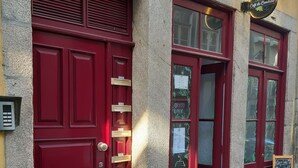A red door with a brass handle, a small sign above the door, and a chalkboard sign on the adjacent wall.