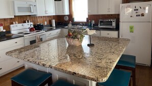 Una cocina con gabinetes blancos, una isla de granito y taburetes azules.