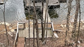 A wooden dock leading to a small wooden platform with a metal railing, surrounded by trees and a body of water.