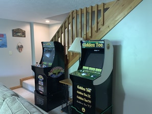 Two arcade machines, a staircase, and a wall with a poster.